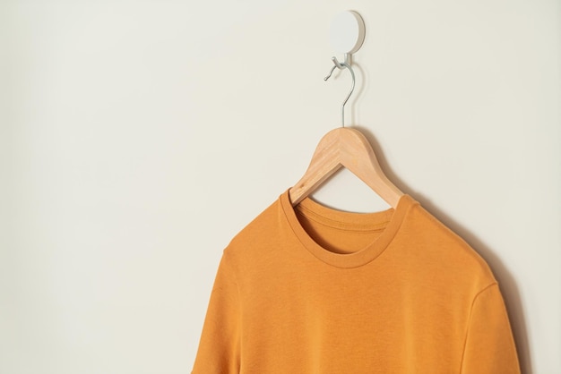 Photo tshirt orange suspendu avec un cintre en bois au mur