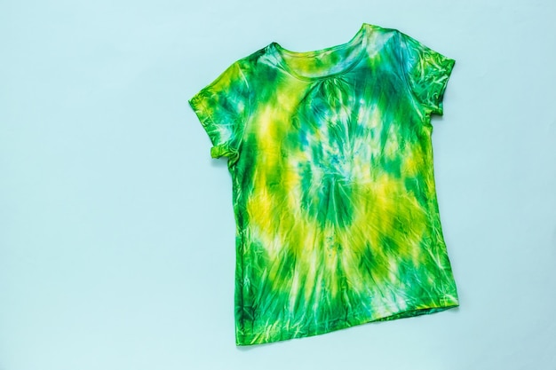 Tshirt en vert jaune et bleu style tie dye sur fond bleu clair Mise à plat