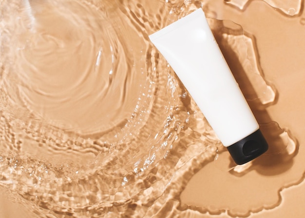 Tuba de crème cosmétique dans de l'eau transparente propre avec la lumière du soleil sur fond beige