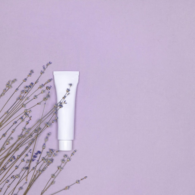 Tube Blanc Crème De Soins De La Peau Avec Des Fleurs De Lavande Sur Fond Violet. Vue De Dessus. Espace De Copie