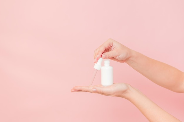 Tube blanc avec pipette avec serum lotion ou huile essentielle acide hyaluronique et collagène dans les mains sur fond rose Cosmétiques de soin de la peau concept flyer de beauté