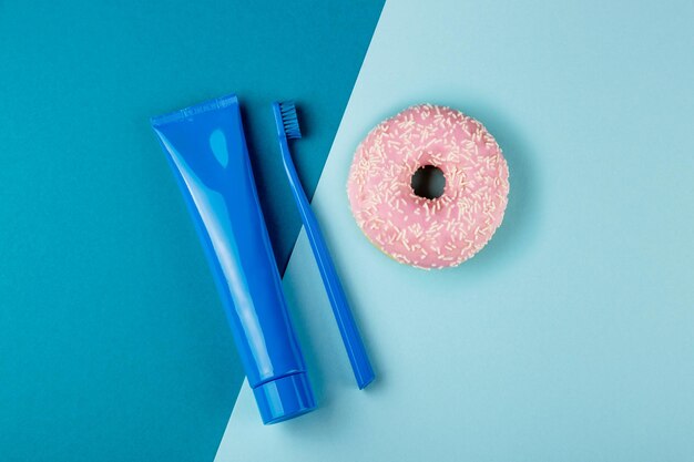 Tube bleu de brosse à dents bleue de dentifrice et beignet rose se trouvent sur la vue de dessus de fond bleu combiné