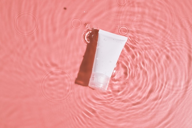 Tube cosmétique blanc sur la surface de l'eau rose Étiquette vierge pour la maquette de marque Vue de dessus à plat