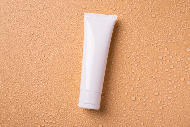 Tube De Crème Blanche Sur Fond Beige Avec Des Gouttes D'eau