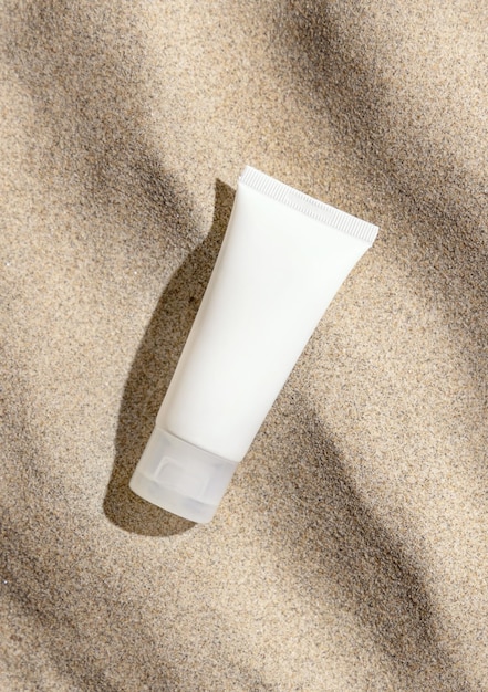 Tube de crème blanche sur sable beige vue de dessus lumière dure Maquette d'emballage cosmétique