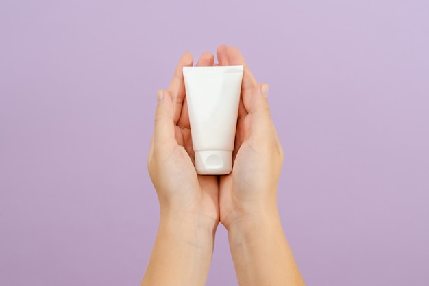 Tube de crème cosmétique dans la main de la femme sur fond lilas Concept de beauté Tube d'emballage pour produits cosmétiquesxA