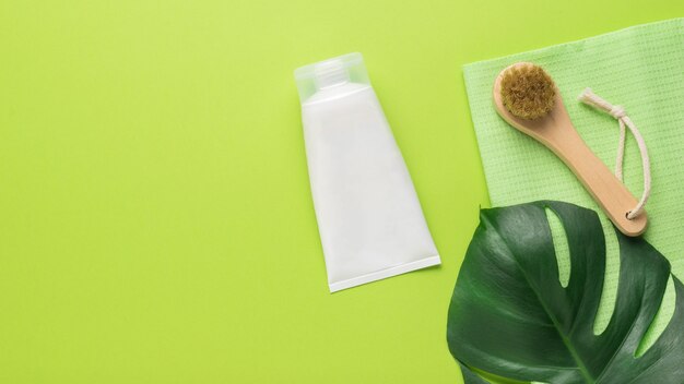 Un tube de crème, une feuille de monstera et une brosse de massage sur fond vert. Spa. Mise à plat.