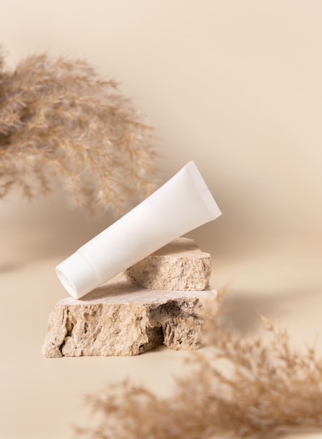Tube de crème en plastique blanc sur pierre près d'herbe de pampa sèche sur maquette beige clair