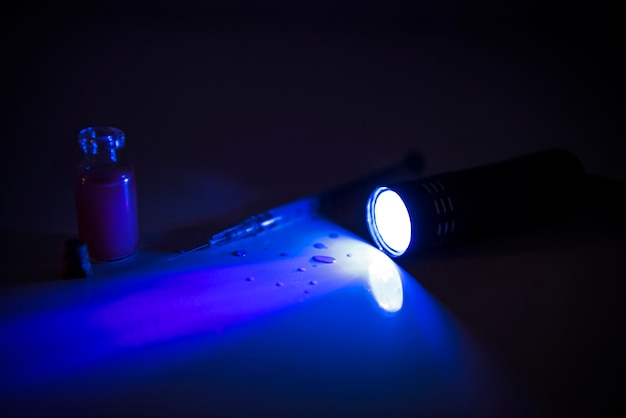 Tube à médicaments et seringue sous lumière ultraviolette. Photo abstraite du temps de la maladie.