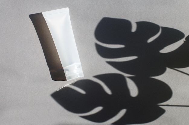 Tube en plastique pour crème ou lotion sur fond gris avec ombre de feuilles de montera Concept de beauté