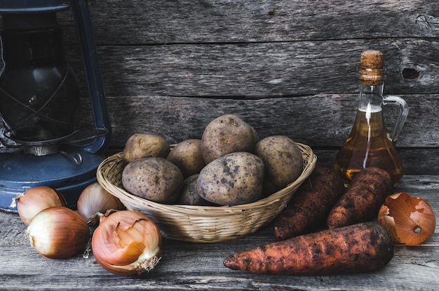 Tubercules de pomme de terre dans un panier carotte et oignon avec de l'huile de tournesol et la vieille lampe à huile sur un fond en bois