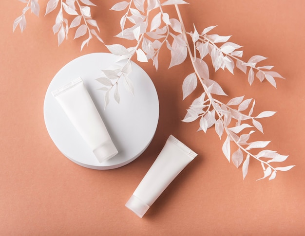 Tubes blancs de crème sur fond marron et branche décorative avec des feuilles blanches