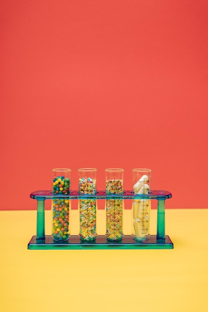 Tubes à essai en verre de laboratoire avec des saupoudres de sucre candi coloré et des pilules de médecine sur fond jaune et rouge avec espace de copie Concept créatif de surdosage placebo et de dépendance aux compléments alimentaires