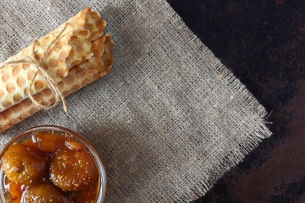 Tubes de plaquette attachés avec de la corde et de la confiture de figues sur une nappe de jute, vue de dessus.