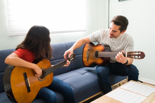 Étude des accords de guitare et des notes de musique. Beau professeur masculin donnant des cours de guitare à une préadolescente à la maison