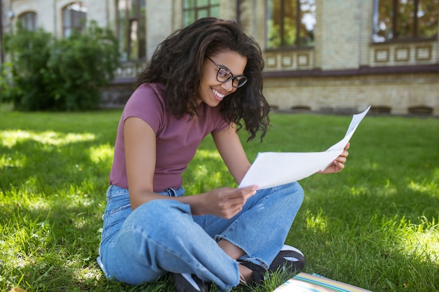 Étude en ligne. Une fille en vêtements décontractés assise sur l'herbe dans le parc et étudiant