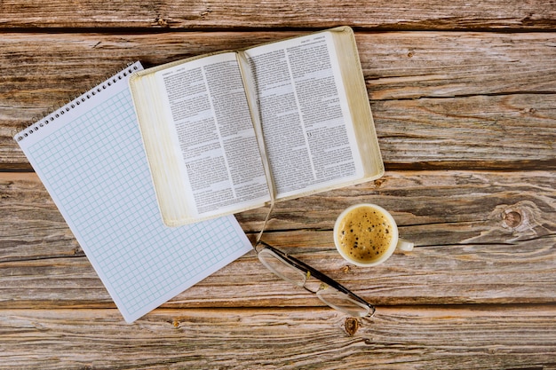 Étude personnelle de la Sainte Bible avec une tasse de café sur un dessus de table avec des lunettes, un bloc-notes en spirale