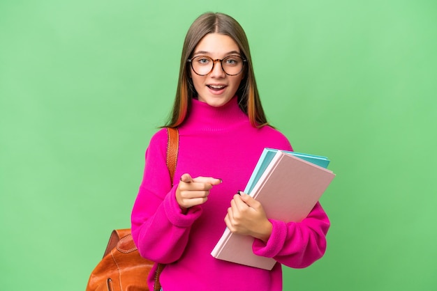 Étudiant adolescent caucasien fille sur fond isolé surpris et pointant vers l'avant