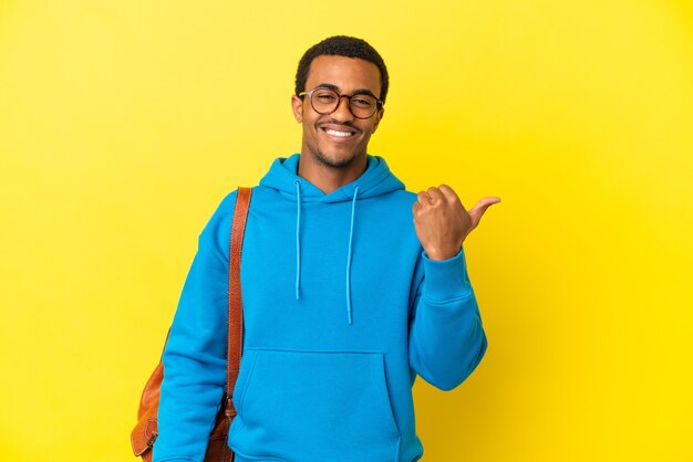 Étudiant afro-américain sur un mur jaune isolé pointant sur le côté pour présenter un produit