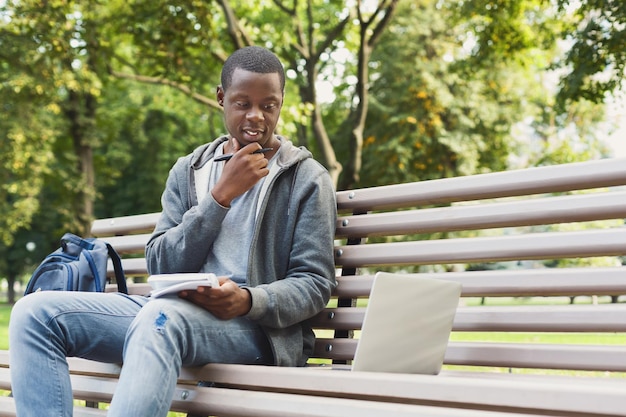 Étudiant afro-américain réfléchi qui étudie et utilise un ordinateur portable avec un ordinateur portable dans le parc. Technologie, communication, éducation et concept de travail à distance, espace de copie