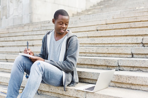 Étudiant afro-américain souriant qui étudie et utilise un ordinateur portable avec un ordinateur portable sur le campus universitaire. Technologie, communication, éducation et concept de travail à distance, espace de copie