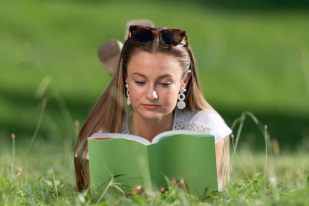 Étudiant assez blond apprenant et lisant un livre s'étendant sur l'herbe