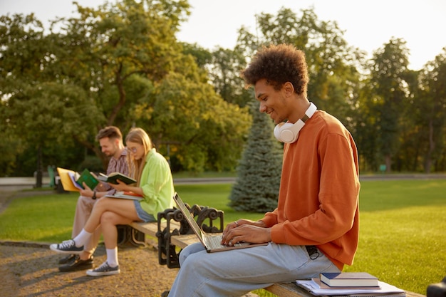 Étudiant assis sur un banc dans le parc universitaire et étudiant sur un ordinateur portable. Concept d'apprentissage et d'éducation