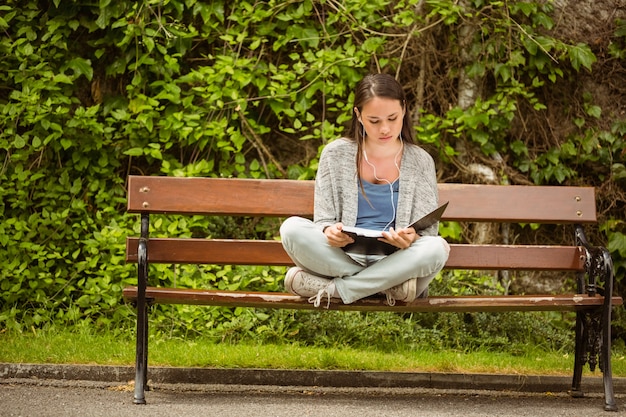 Étudiant assis sur un banc en écoutant de la musique avec un téléphone portable et en révisant dans un parc à l&#39;école
