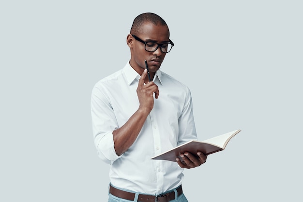 Étudiant. Beau jeune homme africain lisant quelque chose en se tenant debout sur fond gris