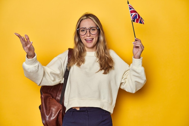 Étudiant britannique portant le drapeau du concept Erasmus sur fond jaune reçoit une agréable surprise excité et lève la main