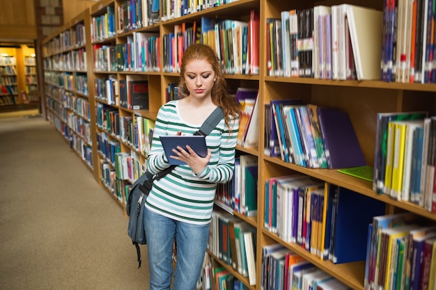 Étudiant ciblé à l&#39;aide de tablette s&#39;appuyant sur une étagère dans la bibliothèque