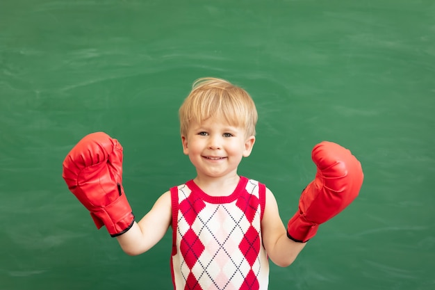 Étudiant enfant drôle portant des gants de boxe rouges en classe contre tableau vert. Éducation physique.