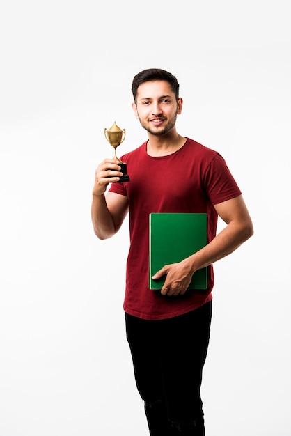 Étudiant indien avec livre, lecture ou montrant la coupe de la victoire, récompense en se tenant isolé sur fond blanc