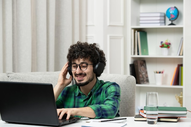 Étudiant en ligne mignon jeune homme étudiant sur ordinateur dans des verres en chemise verte souriant et tapant