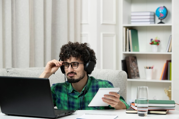 Étudiant en ligne mignon jeune homme étudiant sur ordinateur dans des verres en chemise verte tenant des lunettes