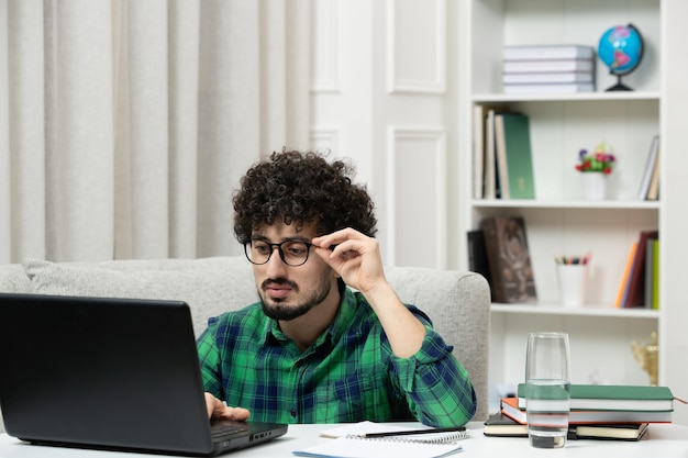 Étudiant en ligne mignon jeune homme étudiant sur ordinateur dans des verres en chemise verte touchant des lunettes