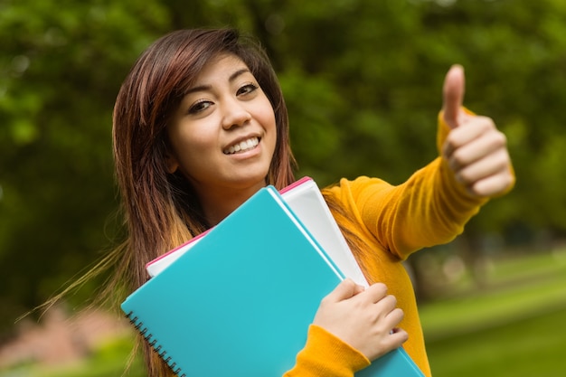 Étudiant avec livres gesticulant pouce en l&#39;air dans le parc