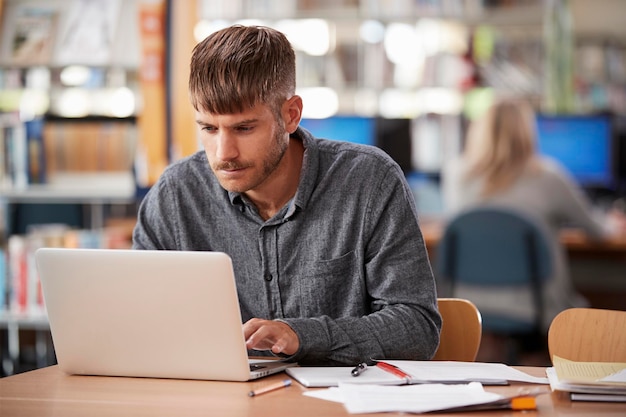 Étudiant mâle mature travaillant sur ordinateur portable dans la bibliothèque du Collège