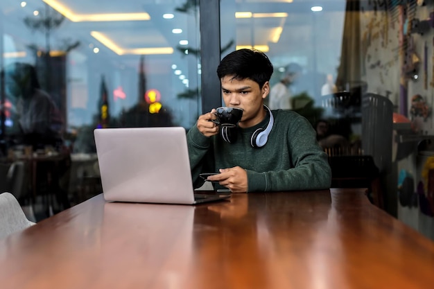 Étudiant masculin asiatique étudiant à l'aide d'un ordinateur portable au café