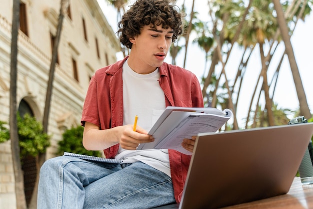 Étudiant masculin regardant attentivement le cahier et l'ordinateur portable tout en apprenant