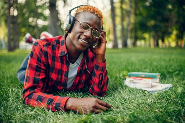 Étudiant noir au casque reposant sur l'herbe dans le parc d'été.