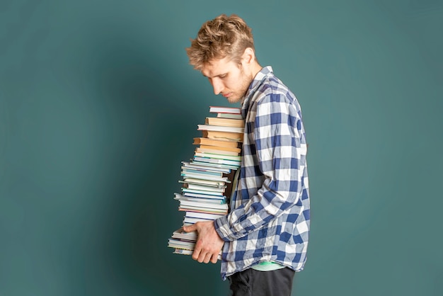 Étudiant occasionnel portent une énorme pile de livres sur fond sombre f