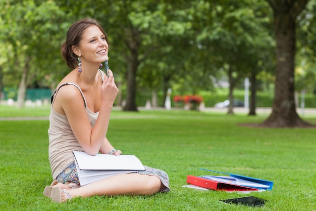 Étudiant réfléchie avec des livres assis au parc