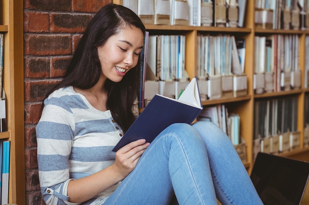 Étudiant souriant, assis sur le sol contre le mur dans le livre de lecture de la bibliothèque