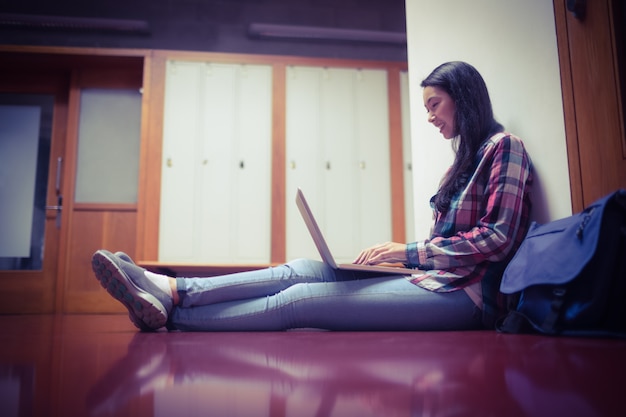 Étudiant souriant, assis sur le sol et utilisant un ordinateur portable