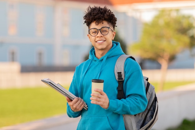 Étudiant souriant tenant des livres et une tasse de café