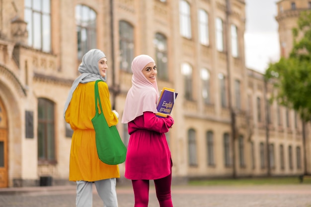 Étudiant tenant des livres. Étudiant musulman souriant tenant des livres marchant vers des cours avec un ami