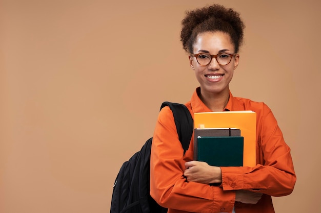 Étudiant universitaire afro-américain à lunettes tenant des livres et un sac à dos isolé sur fond