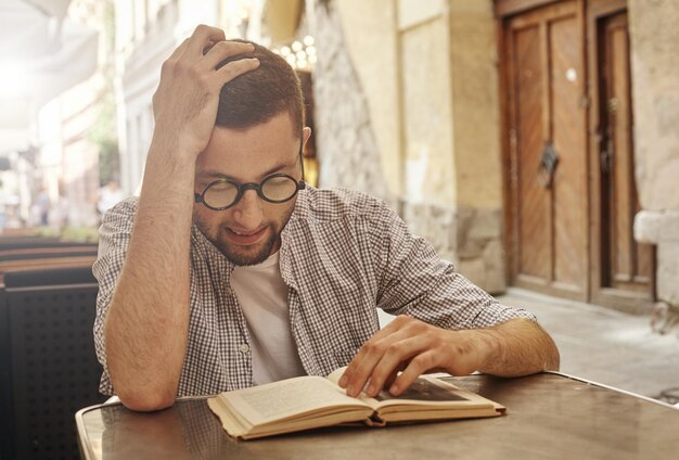 Étudiant universitaire assis et lisant un livre dans la rue dans un café.