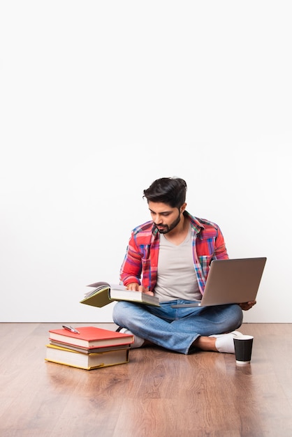 Étudiant d'université ou d'université asiatique indien assis avec un ordinateur portable avec des livres sur un plancher en bois sur fond blanc